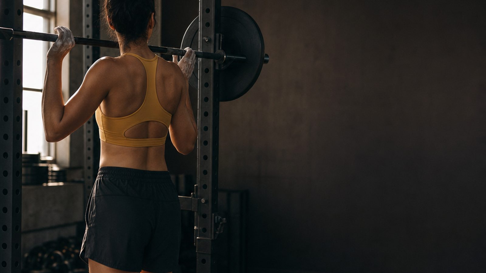 Adult setting up a barbell in an understated strength gym, seen from behind